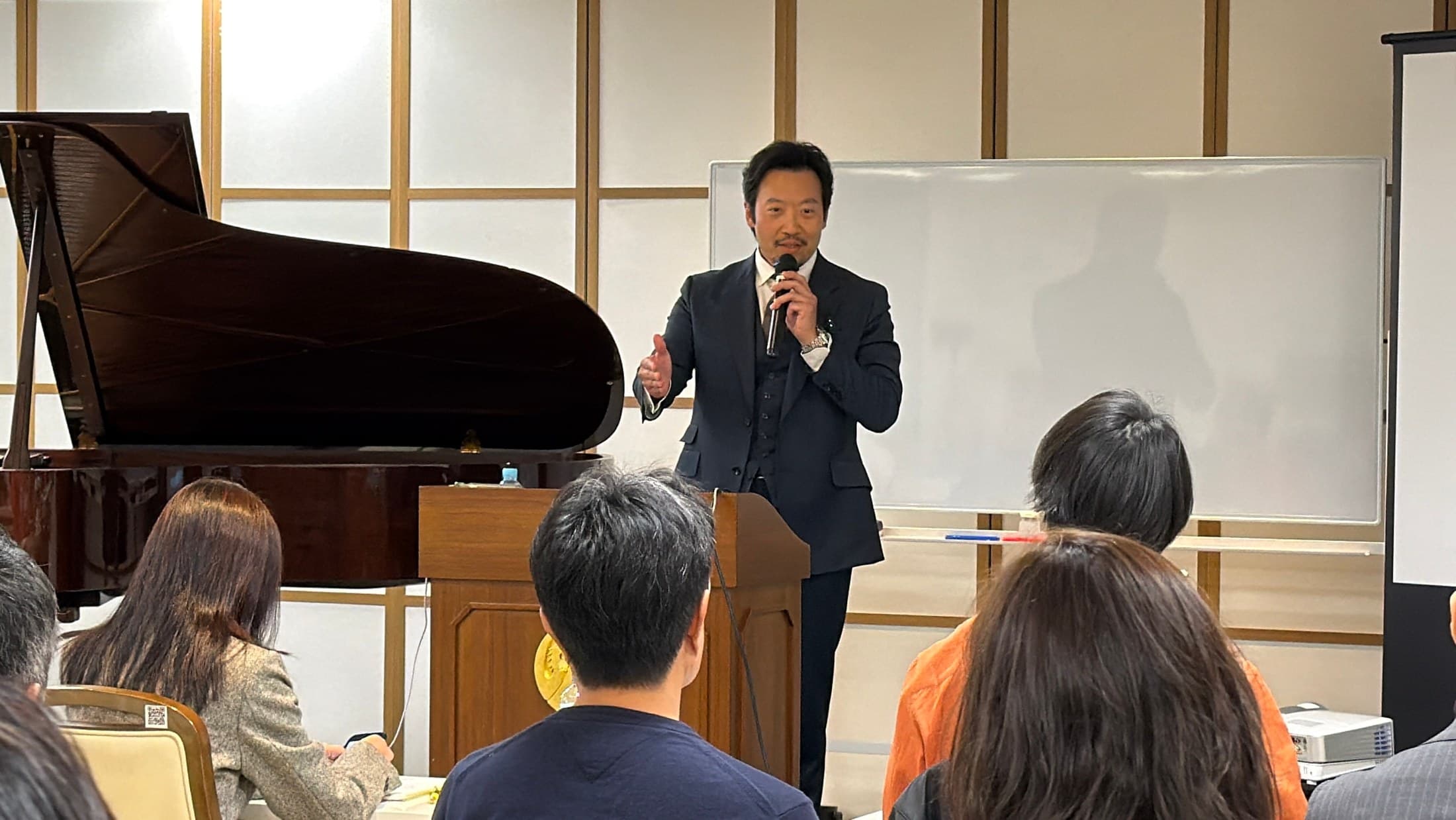 演台で身振りを交えて話す講師と、話を聴く参加者
